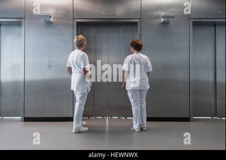 Rear view of nurses in hospital waiting for elevator Stock Photo