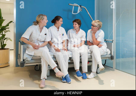 Nurses sitting side by side on bench in hospital, chatting Stock Photo