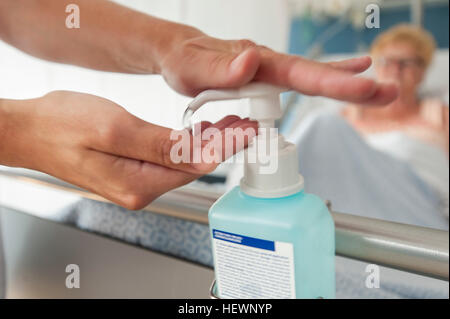 Nurse using hand sanitiser on hospital bed Stock Photo