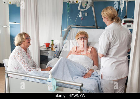 Nurse and visitor tending to patient in hospital bed Stock Photo