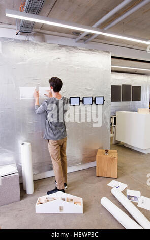 Architect in office looking at blueprint on wall Stock Photo