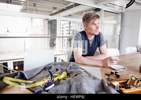 Fashion designer at table holding tea cup looking away Stock Photo