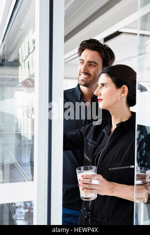 Colleagues in office looking at sticky notes on window Stock Photo