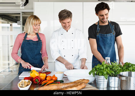 Chef and couple in kitchen slicing vegetables Stock Photo