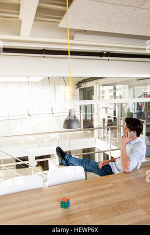 Man in office, legs raised, using mobile phone Stock Photo