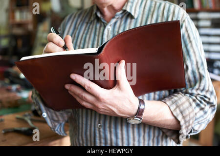 Man in leather workshop, writing in leather bound notebook, mid section, close-up Stock Photo