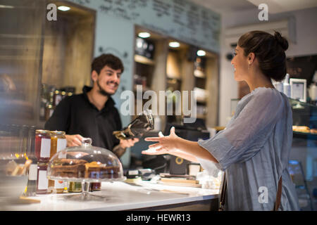 Barista handing baguette to female customer at cafe counter Stock Photo