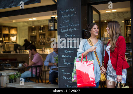 Two young female friends outside cafe carrying shopping bags Stock Photo