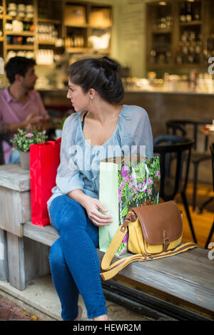 Young woman shopper sitting outside cafe looking over her shoulder