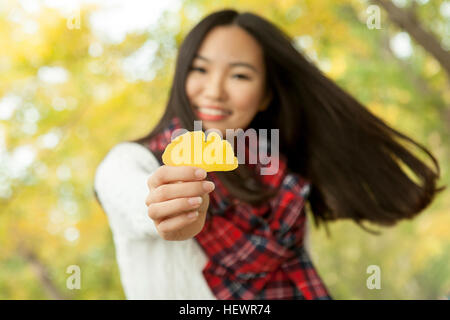 Portrait of young woman holding yellow gingko leaf in autumn park, Beijing, China Stock Photo