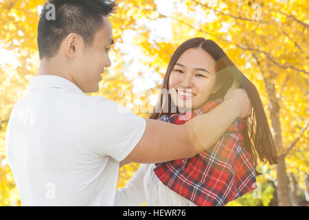 Young man wrapping tartan scarf around girlfriend in autumn park, Beijing, China Stock Photo