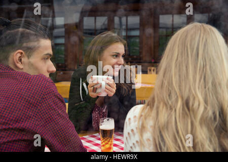 Three young adult friends with herbal tea and beer in cafe Stock Photo