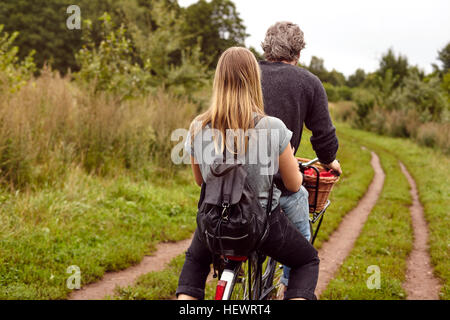 Rear view of couple riding bicycle on rural dirt track Stock Photo