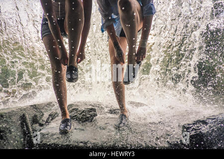 Waist down of girls on rock by waterfall putting on shoes Stock Photo