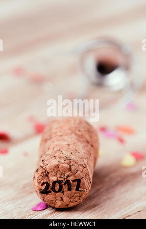 the number 2017, as the new year, written in the cork of a bottle of champagne, on a wooden table full of confetti Stock Photo