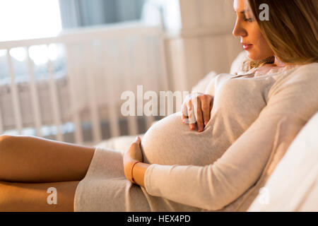 Pretty young pregnant woman lying on the bed in room Stock Photo