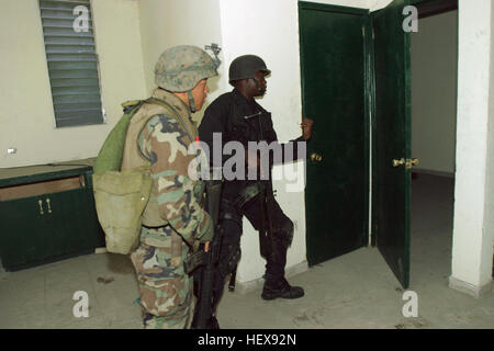 A US Marine Corps (USMC) Marine assigned to 3/8 Kilo Company, 1st Platoon, 2nd Marine Division, armed with a 5.56mm M16A2 rifle, accompanies a member of the Haitian National Police Special Weapons And Tactics  (HNP SWAT) team, armed with a 5.56mm Vektor R5 assault rifle, equipped with folding stock, during the search an apartment complex during a pre-dawn raid. The complex was believed to be the location where Marines had been taking sporadic fire from since they arrived in Port-Au Price, Haiti. USMC Marines with Haitian National Police, who translate and enforce Haitian laws, conduct raids to Stock Photo