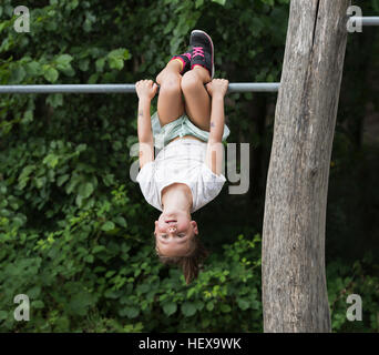 Girl hanging upside down from monkey bar Stock Photo