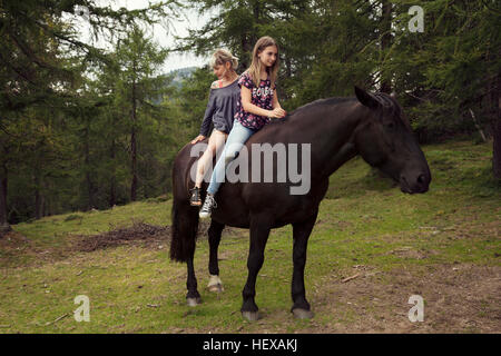 Girl and woman sitting bareback on horse in forest glade, Sattelbergalm, Tyrol, Austria Stock Photo