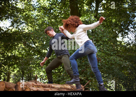 Couple in forest holding hands balancing on fallen tree Stock Photo