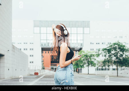 Young woman listening to headphones with hand on head outside office building Stock Photo