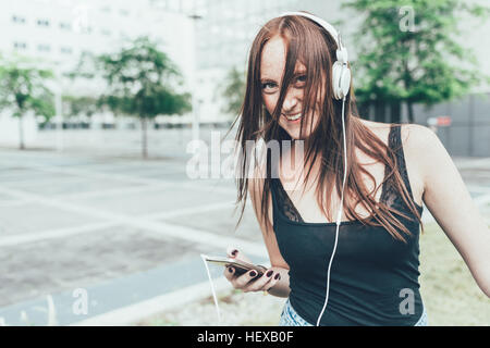Portrait of young woman listening to headphones and dancing outside office building Stock Photo