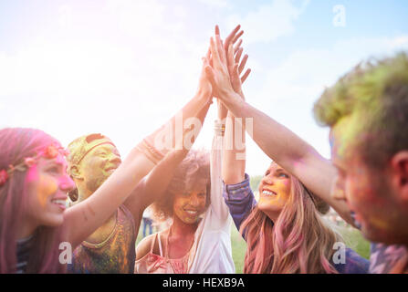 Group of friends at festival, covered in colourful powder paint, joining hands Stock Photo