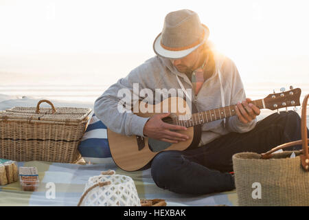 Young man playing guitar on sunlit beach, Cape Town, Western Cape, South Africa Stock Photo