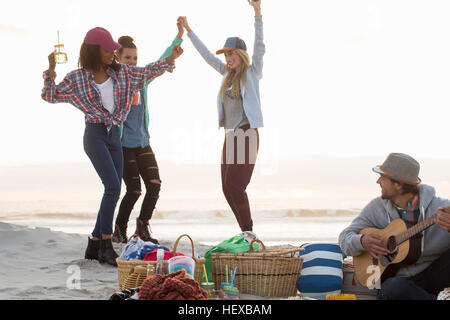 Young man playing guitar and female friends dancing at beach, Cape Town, Western Cape, South Africa Stock Photo