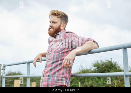 Man leaning against farm gate looking away Stock Photo