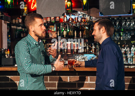 two young man talking at counter.  friends standing in bar and drinking whisky Stock Photo