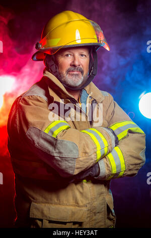 Portrait of a fireman wearing Fire Fighter turnouts and helmet. Background is red and blue smoke and light. Turnouts are protect Stock Photo