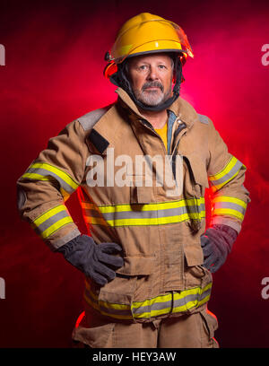 Portrait of a fireman wearing Fire Fighter turnouts and helmet. Background is red and blue smoke and light. Turnouts are protect Stock Photo