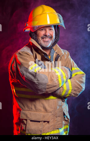 Portrait of a fireman wearing Fire Fighter turnouts and helmet. Background is red and blue smoke and light. Turnouts are protect Stock Photo