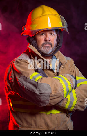 Portrait of a fireman wearing Fire Fighter turnouts and helmet. Background is red and blue smoke and light. Turnouts are protect Stock Photo