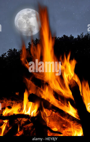 A bonfires burns at night in the woods, under a full moon Stock Photo