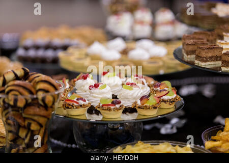 Selection of cream, chocolate and pastry desserts on footed glass cake stands at party, on black tablecloth Stock Photo