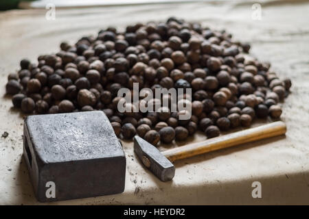 Whole walnuts on old table with anvil and nutcracker hammer Stock Photo