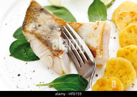 Seafood dish: fork dividing a piece of zander filet, roasted potatoes and spinach leaves Stock Photo