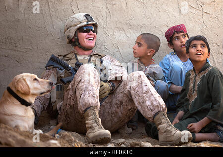 U.S. Marine Lance Cpl. Isaiah Schult, a dog handler with Jump Platoon, Headquarters and Service Company, 3rd Battalion, 3rd Marine Regiment, and 20-year-old Indianapolis native, jokes with Afghan children while providing security with Big, an improvised explosive device detection dog, during a shura outside a local residence here, Nov. 22, 2011. On deployment in Helmand province’s Garmsir district, the ‘America’s Battalion’ dog handlers and their improvised explosive device detection dogs live, travel and work together. In a combat environment largely devoid of the safety and comforts of home, Stock Photo