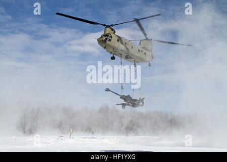 An M-177 155mm howitzer is transported by a CH-47 Chinook during cold weather sling load operations at Camp Grayling Joint Maneuver Training Center, Mich., Feb 28, 2014. (Michigan National Guard photo by Staff Sgt. Kimberly Bratic/Released) Michigan National Guard conducts cold weather sling load and howitzer live fire exercise 140228-Z-LE308-008 Stock Photo