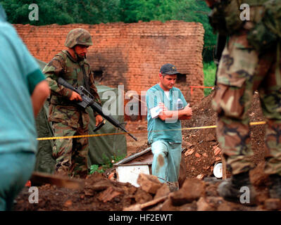 990701-M-5696S-003 U.S. Marines provide security as members of the Royal Canadian Mounted Police Forensics Team investigate a grave site in a village in Kosovo on July 1, 1999.  Elements of the 26th Marine Expeditionary Unit are deployed from ships of the USS Kearsarge Amphibious Ready Group as an enabling force for KFOR.  KFOR is the NATO-led, international military force which will deploy into Kosovo on a peacekeeping mission known as Operation Joint Guardian.  KFOR will ultimately consist of over 50,000 troops from more than 24 contributing nations, including NATO member-states, Partnership Stock Photo