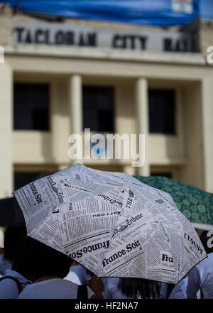 A women uses an umbrella to shade her from the sun during a morning flag raising ceremony in front of the Tacloban City Hall in Tacloban, Leyte, Philippines, Nov. 17, 2014. The flag raising ceremony is a way for the citizens of Tacloban to honor their nation and their city while also receiving updated information on any important topics pertaining to the city. A year after the relief and recovery efforts of Operation Damayan, following the catastrophic destruction caused by Super Typhoon Yolanda across portions of the Philippines, the people of Tacloban, one of the hardest hit areas, have cont Stock Photo