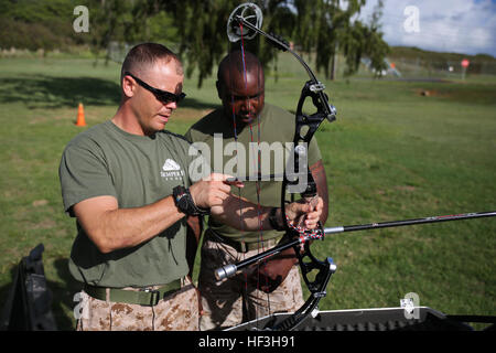 Staff Sgt. Charles Amerson, a section leader with the Wounded Warrior Battalion West-Detachment Hawaii and Tampa, Fla., native, familiarizes Staff Sgt. Terry Hicks, a service member recovering with the Wounded Warrior Detachment and a Washington, D.C., native, with shooting a bow at the archery range aboard Marine Corps Base Hawaii, July 23, 2015. Every Tuesday and Thursday, service members with the detachment participate in activities such as archery, swimming, track, shooting and cycling as part of the Warrior Athletic Reconditioning Program. The purpose of WARP is to help service members fi Stock Photo