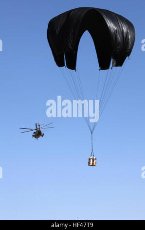 Marines test a new way of delivering emergency supplies to troops on the battlefield with an old method of delivery.  A CH-53D Sea Stallion with Marine Heavy Helicopter Squadron 363 flies away as a test bundle gradually float safely to the ground.  Marines with 3rd Marine Aircraft Wing (Forward) and 1st Marine Logistics Group (Forward) are pushing bundles of water out of the Osprey, CH-53D Sea Stallion and CH-53E Super Stallion using Low Cost Low Altitude Parachutes to float them to the ground safely and a honecombed cardboard cushion for a soft landing.  If this proves effective, the Marines  Stock Photo