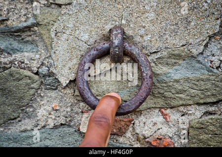 finger pulls an old rusty iron ring that acts as the bell of the old stone and brick wall Stock Photo