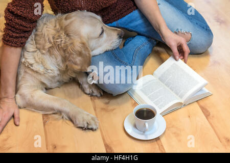 Aerial view of woman sitting down on the floor with Golden retriever dog. Open book and white cup of coffee are lying in front of them. T Stock Photo