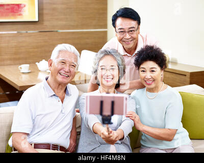 two happy senior asian couples taking a selfie using cellphone on a stick.