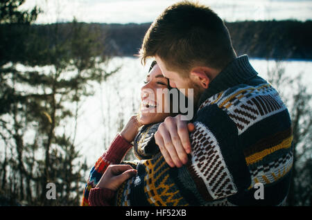 Joyful cute couple embraces. Young man in a sweater hugs a girl from behind background in winter. Stock Photo