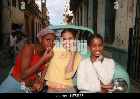 Three pretty girls laughing, standing in front of a vintage car in Havana, Cuba, Caribbean, Americas Stock Photo